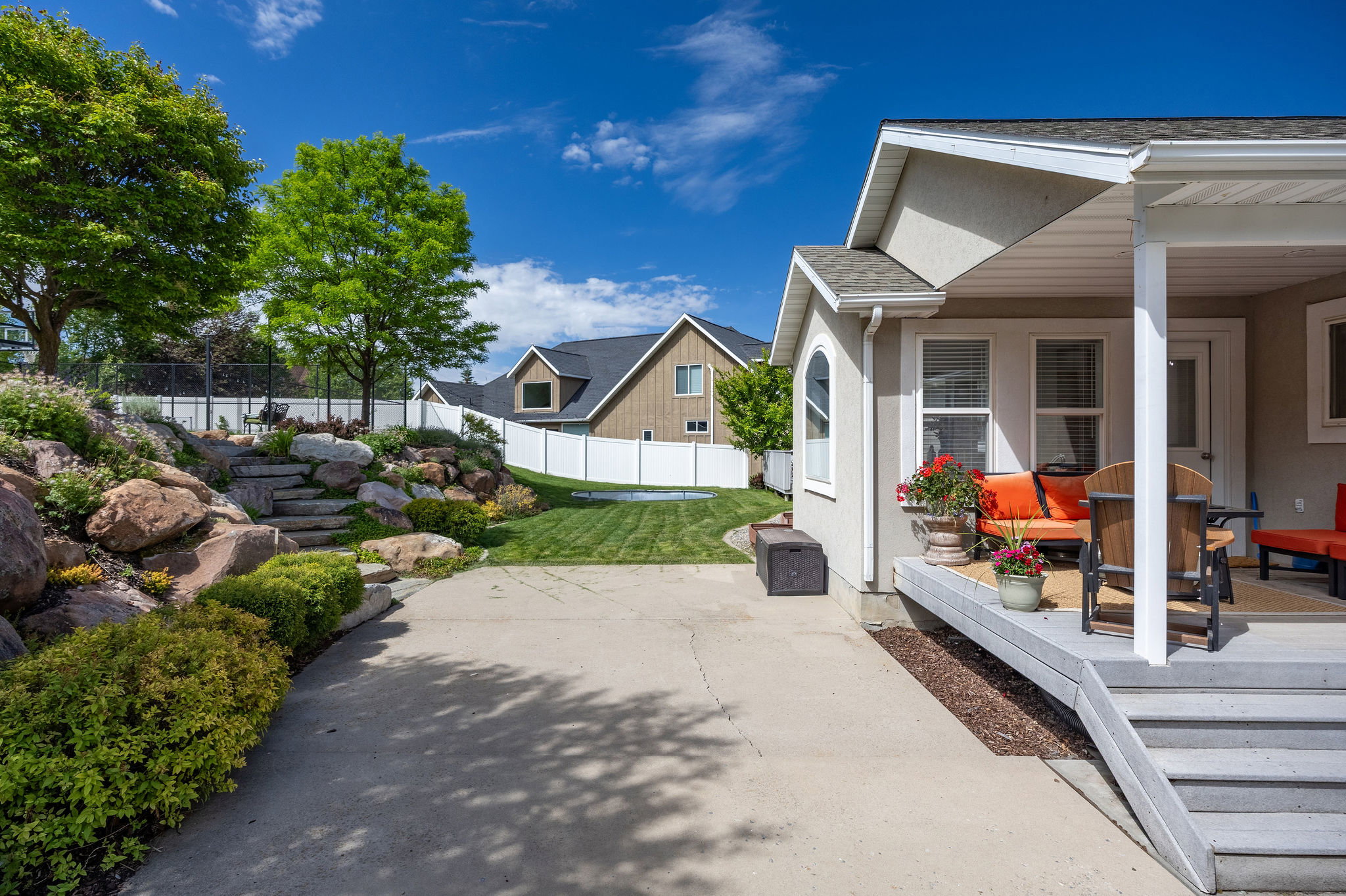Spacious backyard featuring a concrete patio, tiered rock landscaping, and a manicured lawn