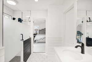 Bathroom featuring a glass-enclosed shower with frosted panel, hexagonal floor tiling, a white vanity with integrated sink, and a matte black faucet