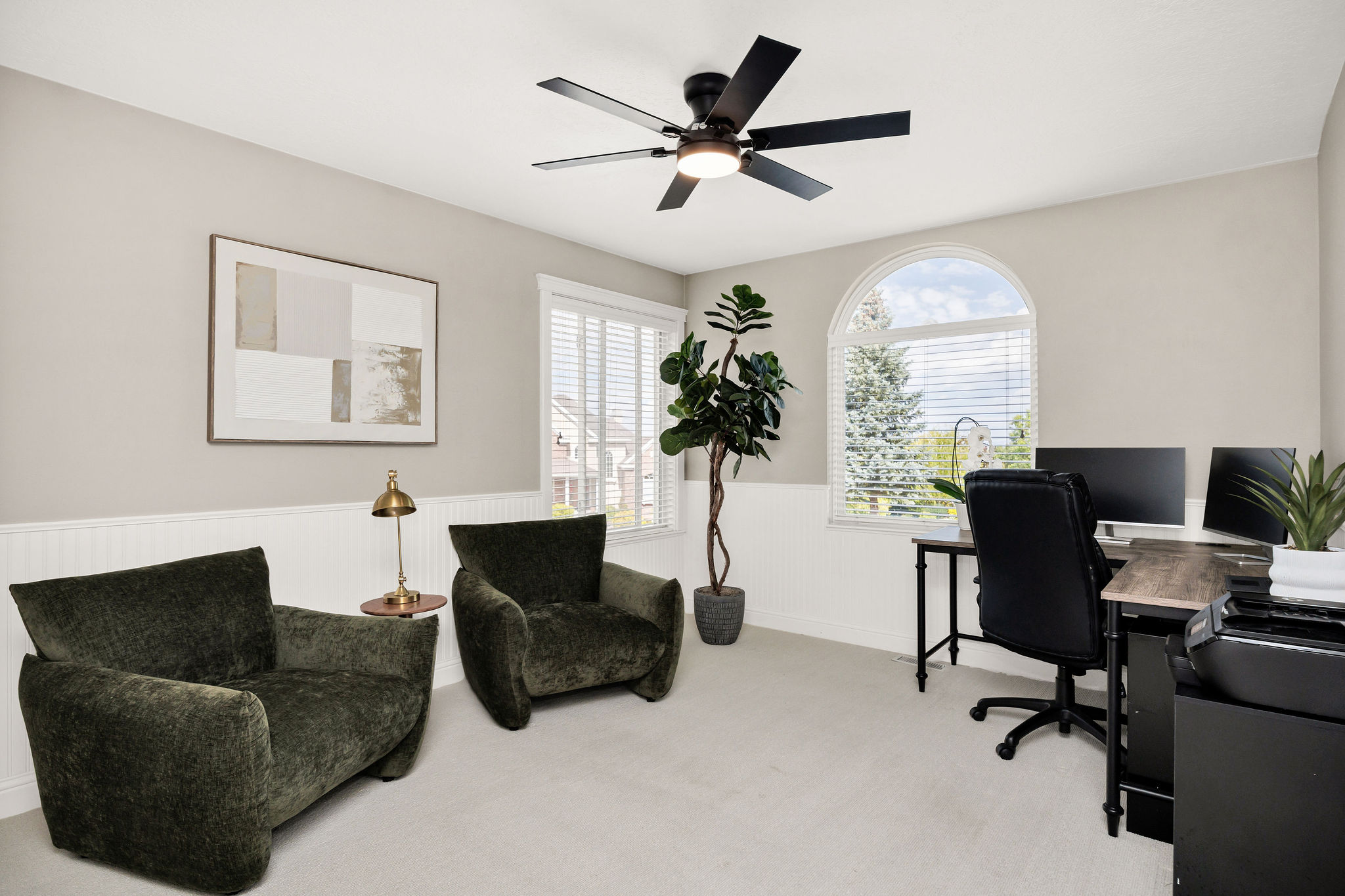 Carpeted room featuring a ceiling fan with integrated lighting, white wainscoting, and an arched window