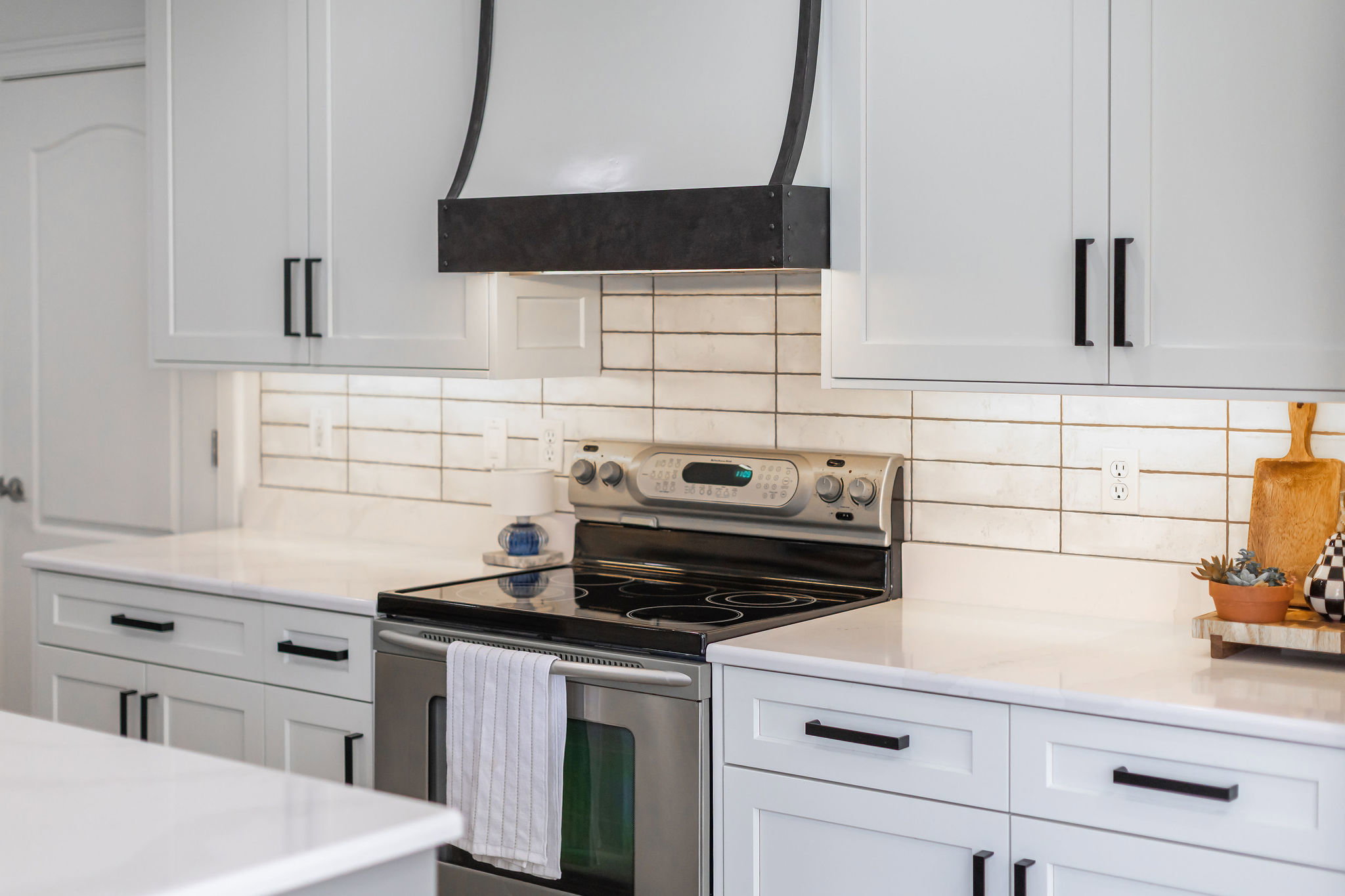 Kitchen featuring white shaker-style cabinetry, a built-in range, and a custom dark-finished range hood