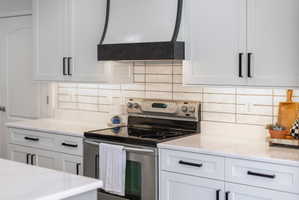 Kitchen featuring white shaker-style cabinetry, a built-in range, and a custom dark-finished range hood