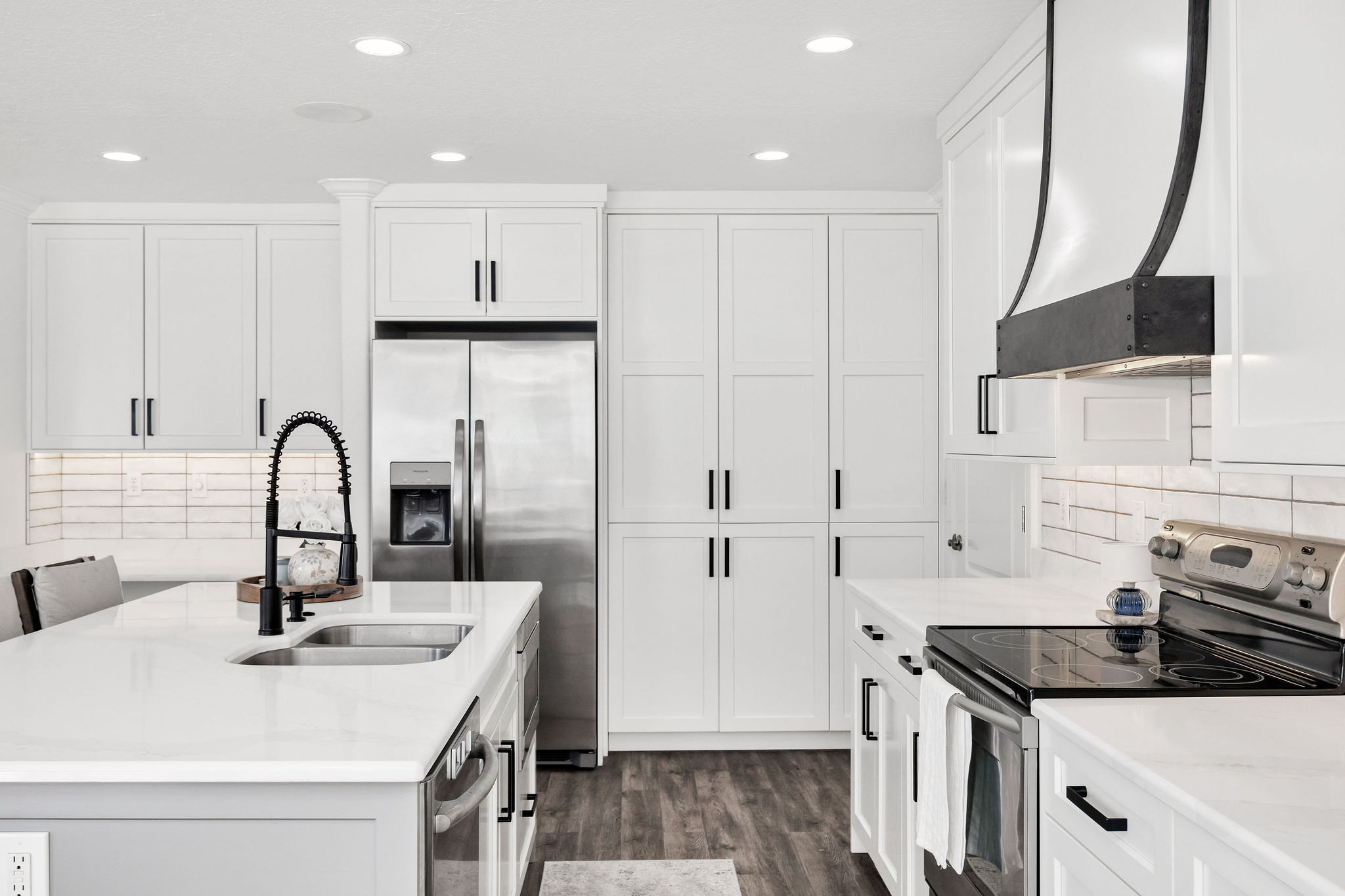 Modern kitchen featuring white cabinetry, stainless steel appliances, a large island with an undermount sink, a black gooseneck faucet, and wood-finish flooring