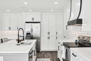 Modern kitchen featuring white cabinetry, stainless steel appliances, a large island with an undermount sink, a black gooseneck faucet, and wood-finish flooring