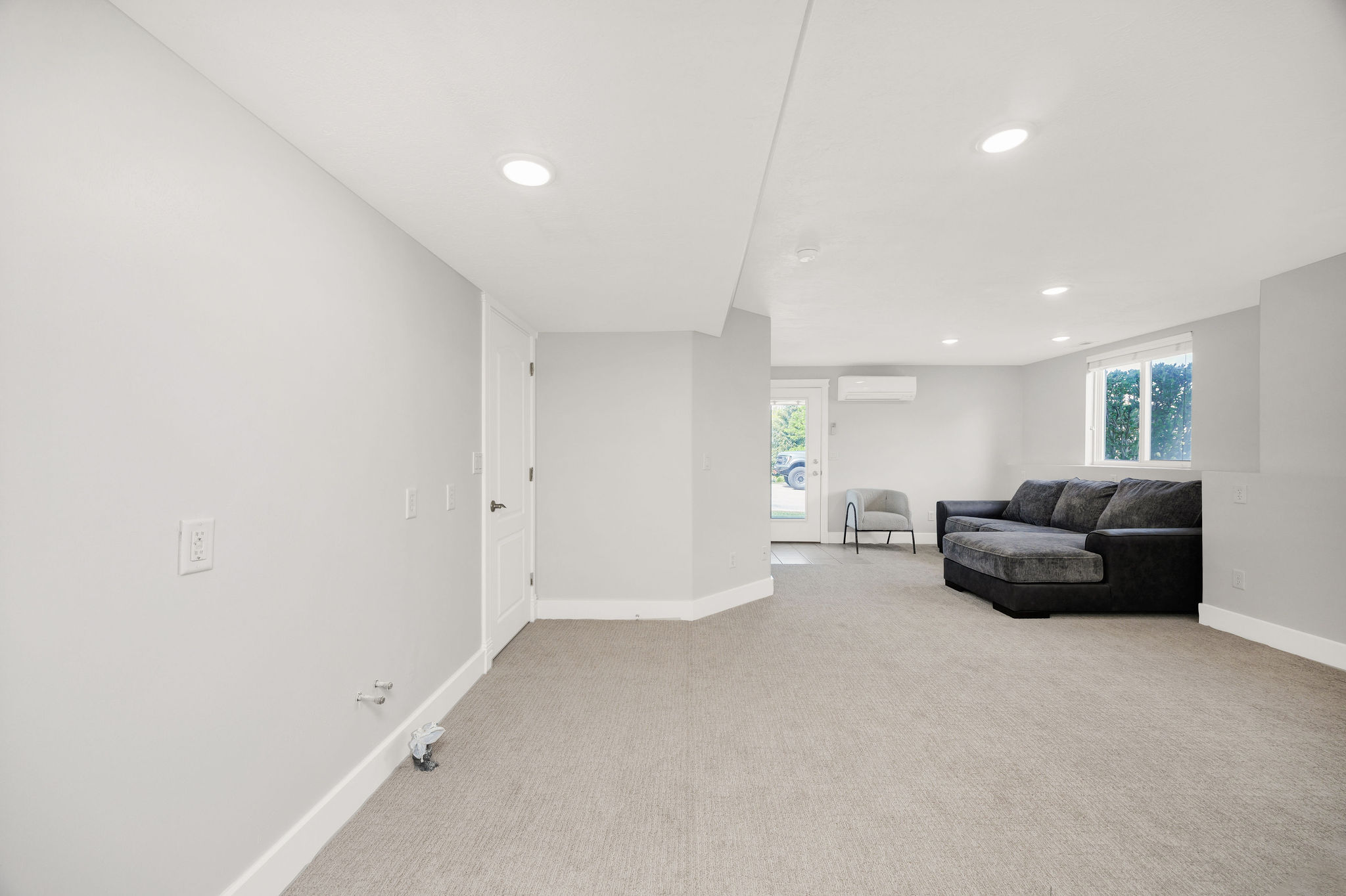 Spacious room featuring light gray walls, recessed lighting, gray carpet flooring, a white trim package, and a white door with dark hardware
