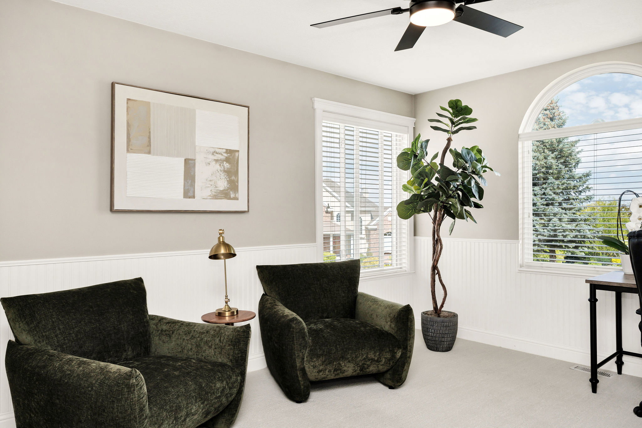 Bright room featuring multiple windows with horizontal blinds, a large arched window, a black ceiling fan with an integrated light, and white wainscoting