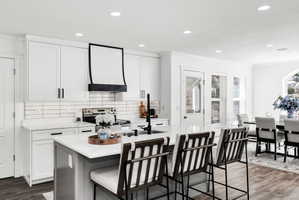 Kitchen featuring white shaker cabinetry, an island with seating, dark wood-finish flooring, recessed lighting, and a white subway tile backsplash
