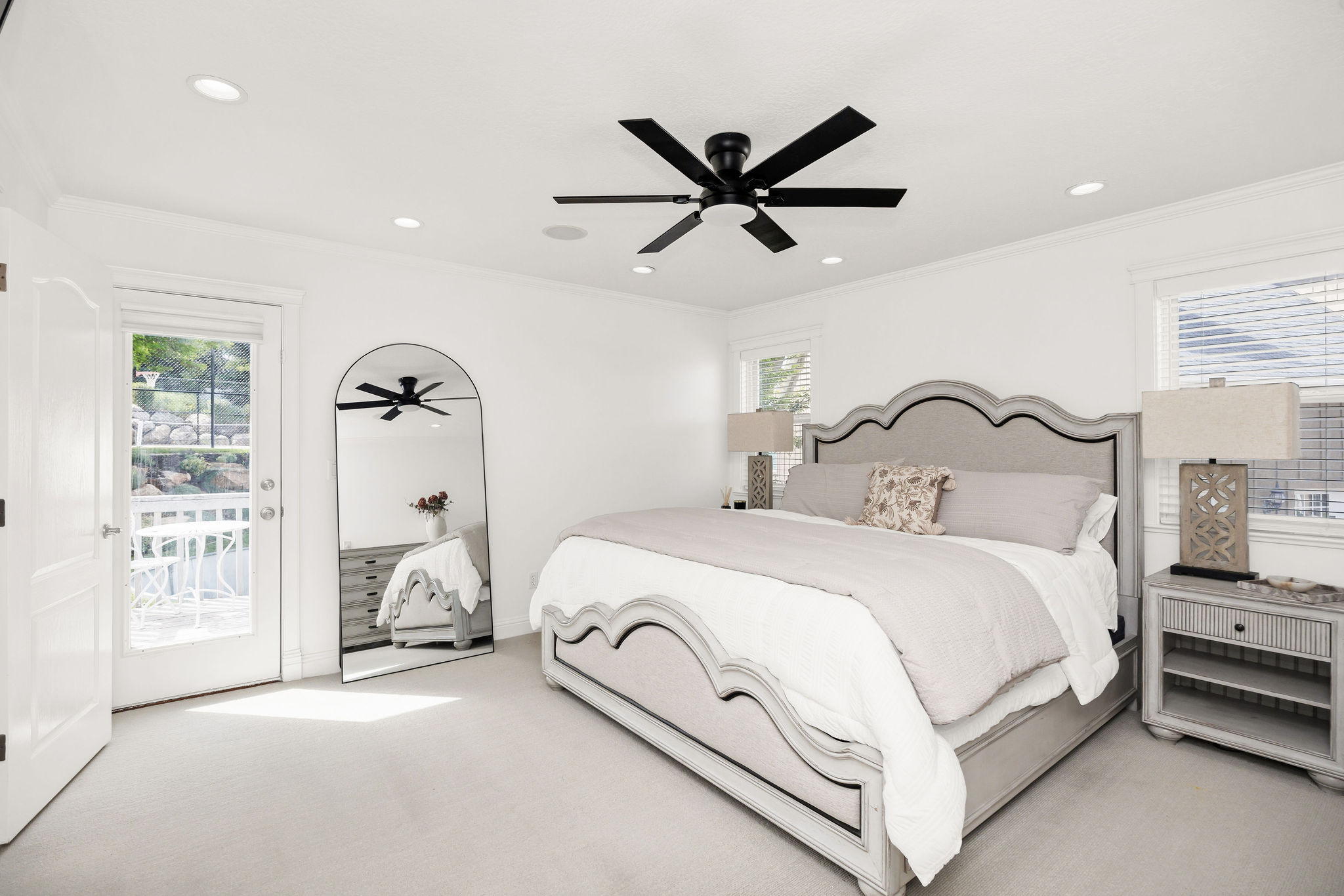 White-painted bedroom featuring light-colored carpeting, a black ceiling fan, recessed lighting, and a glass-paned door opening to an exterior balcony with white railings