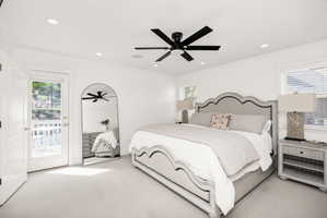 White-painted bedroom featuring light-colored carpeting, a black ceiling fan, recessed lighting, and a glass-paned door opening to an exterior balcony with white railings