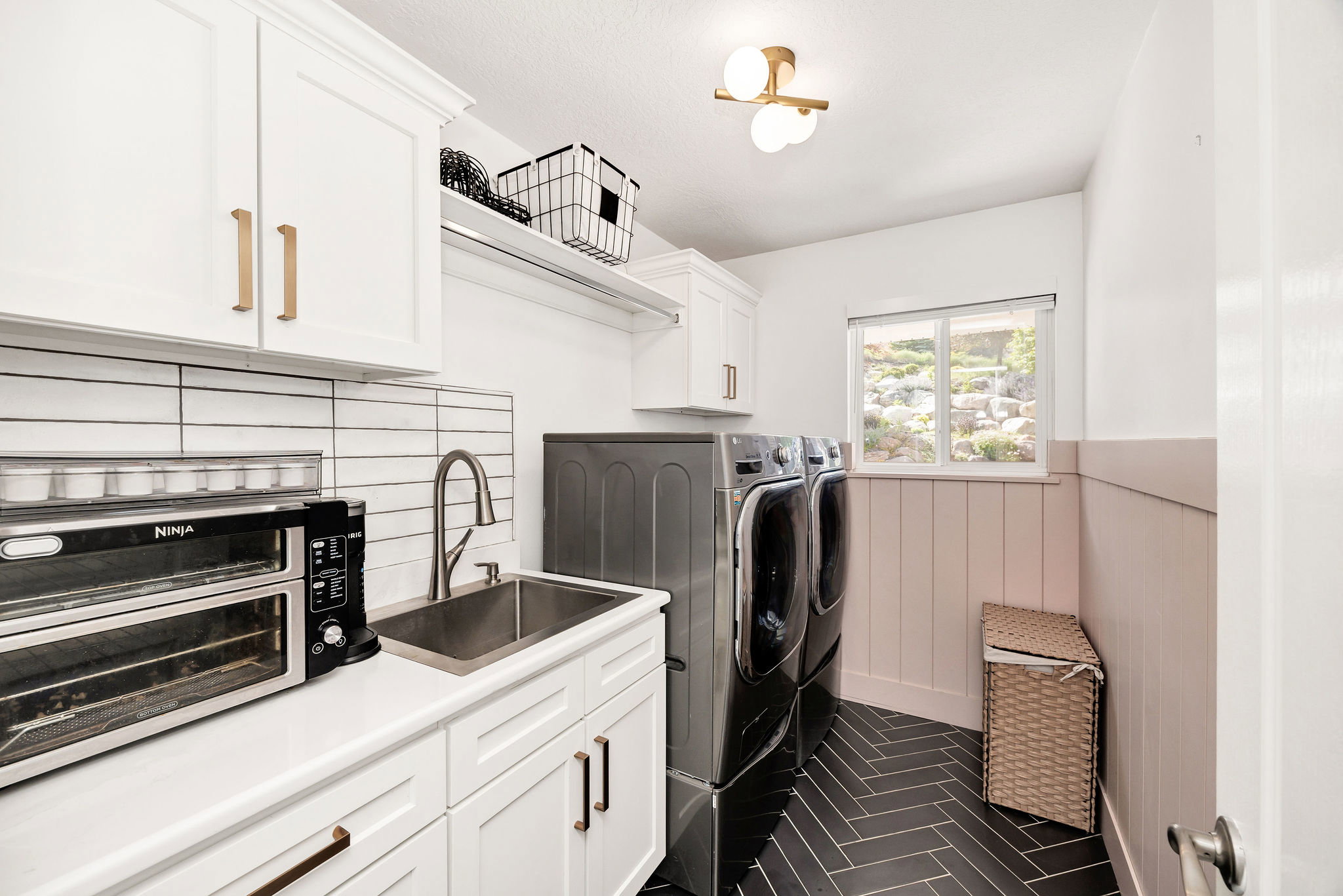 Dedicated laundry area featuring white cabinetry with gold-tone hardware, a stainless steel sink, and a white subway tile backsplash