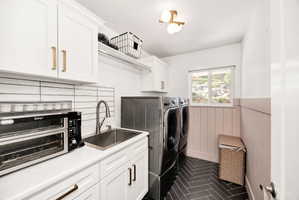 Dedicated laundry area featuring white cabinetry with gold-tone hardware, a stainless steel sink, and a white subway tile backsplash