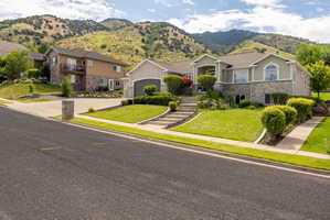 Stucco and stone exterior home featuring an arched entry, a two-car garage, and established landscaping with mature shrubs