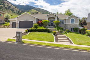 Split-level residence featuring a stucco and stone exterior, a concrete driveway leading to a two-car garage and an additional single-car garage, and a tiered front lawn with concrete steps leading to the main entrance