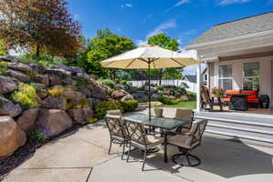 Spacious concrete patio with tiered rock landscaping featuring mature trees and diverse plantings