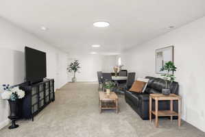 Open-concept living area featuring light-toned carpet flooring and white walls