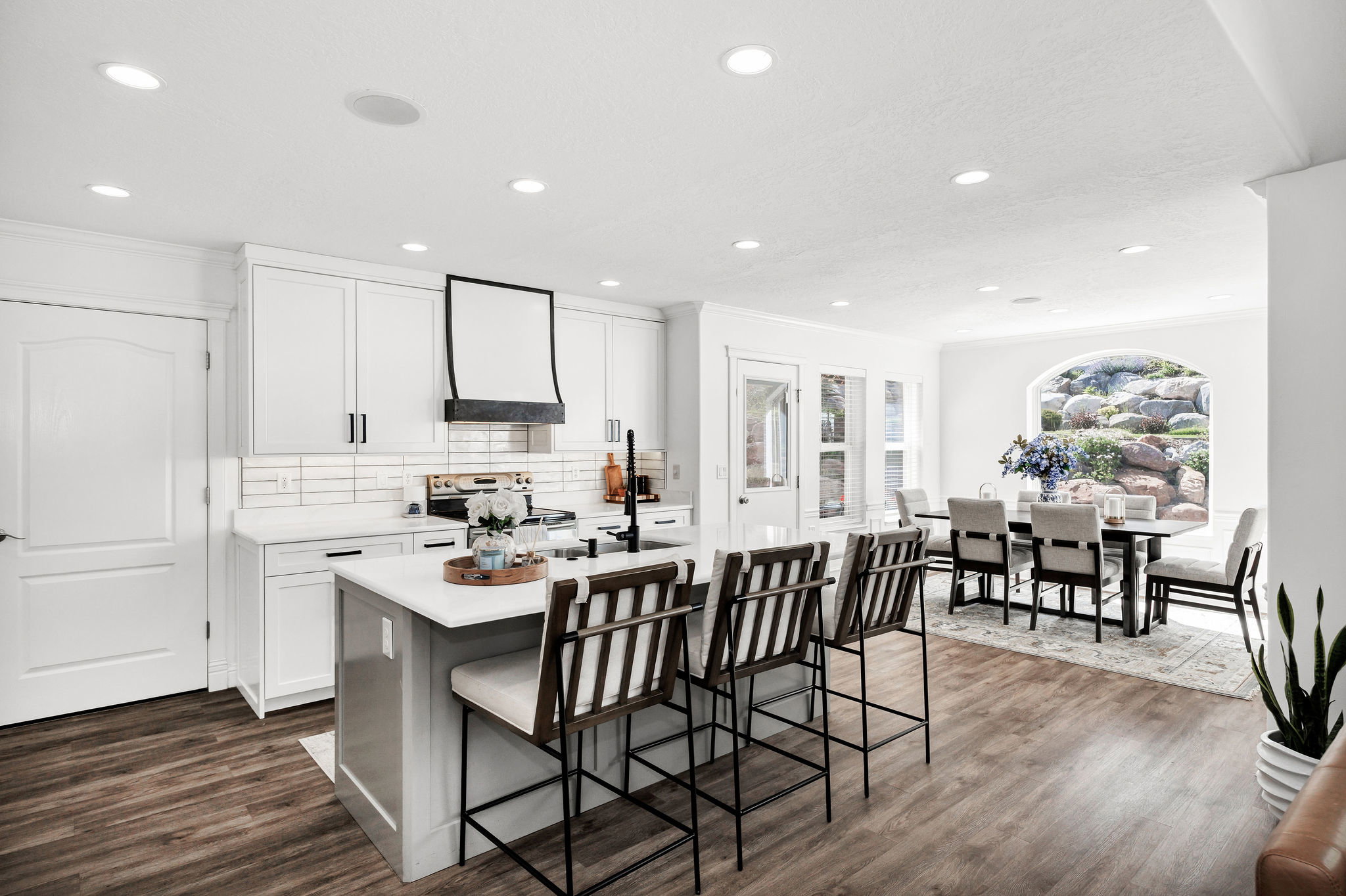 Open-concept kitchen and dining area featuring wood-finish flooring, white cabinetry, a kitchen island with seating, a tile backsplash, and recessed lighting