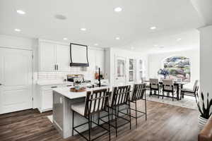 Open-concept kitchen and dining area featuring wood-finish flooring, white cabinetry, a kitchen island with seating, a tile backsplash, and recessed lighting