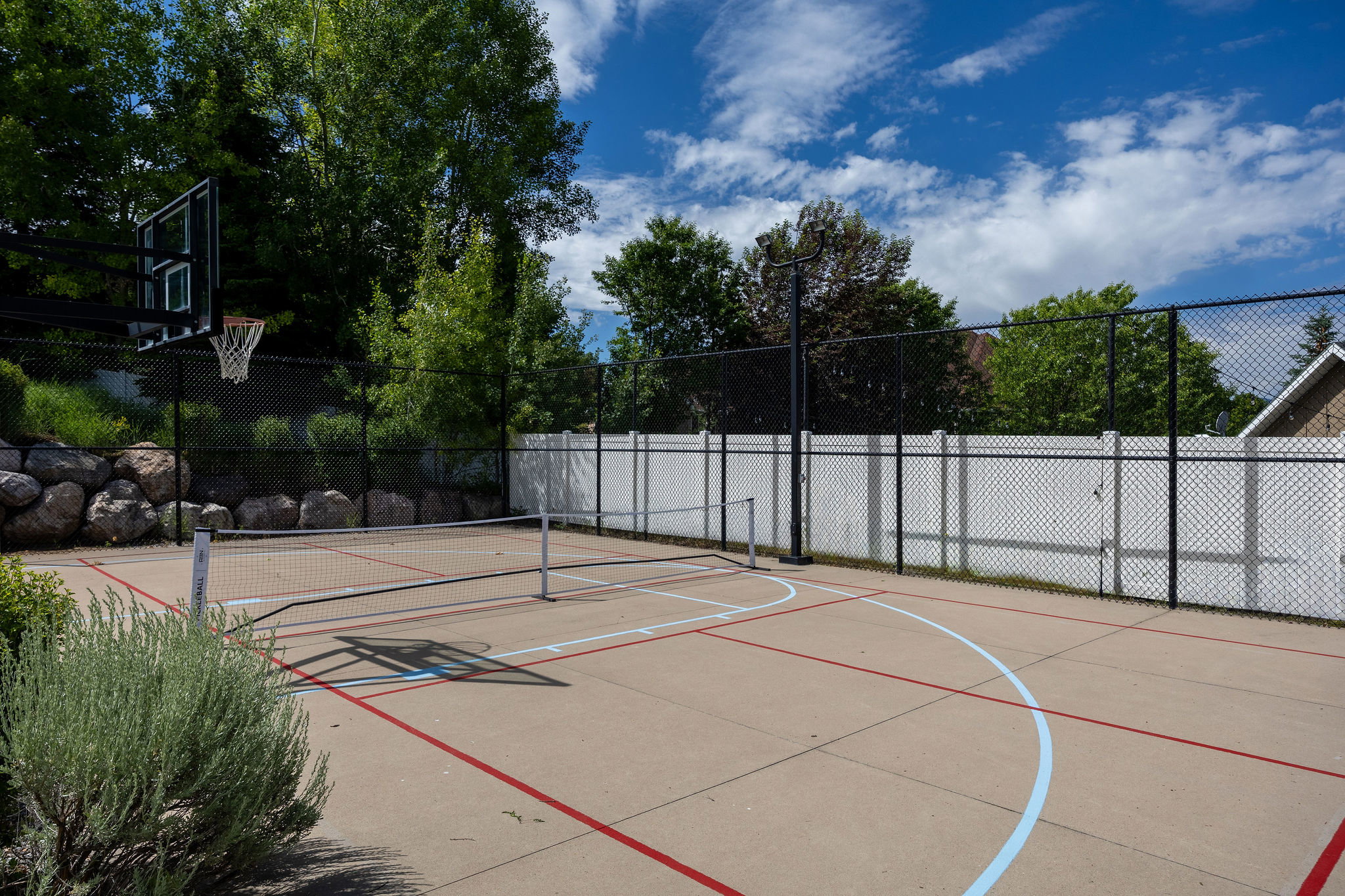 Multi-sport court featuring concrete surfacing, painted court lines, and a basketball hoop
