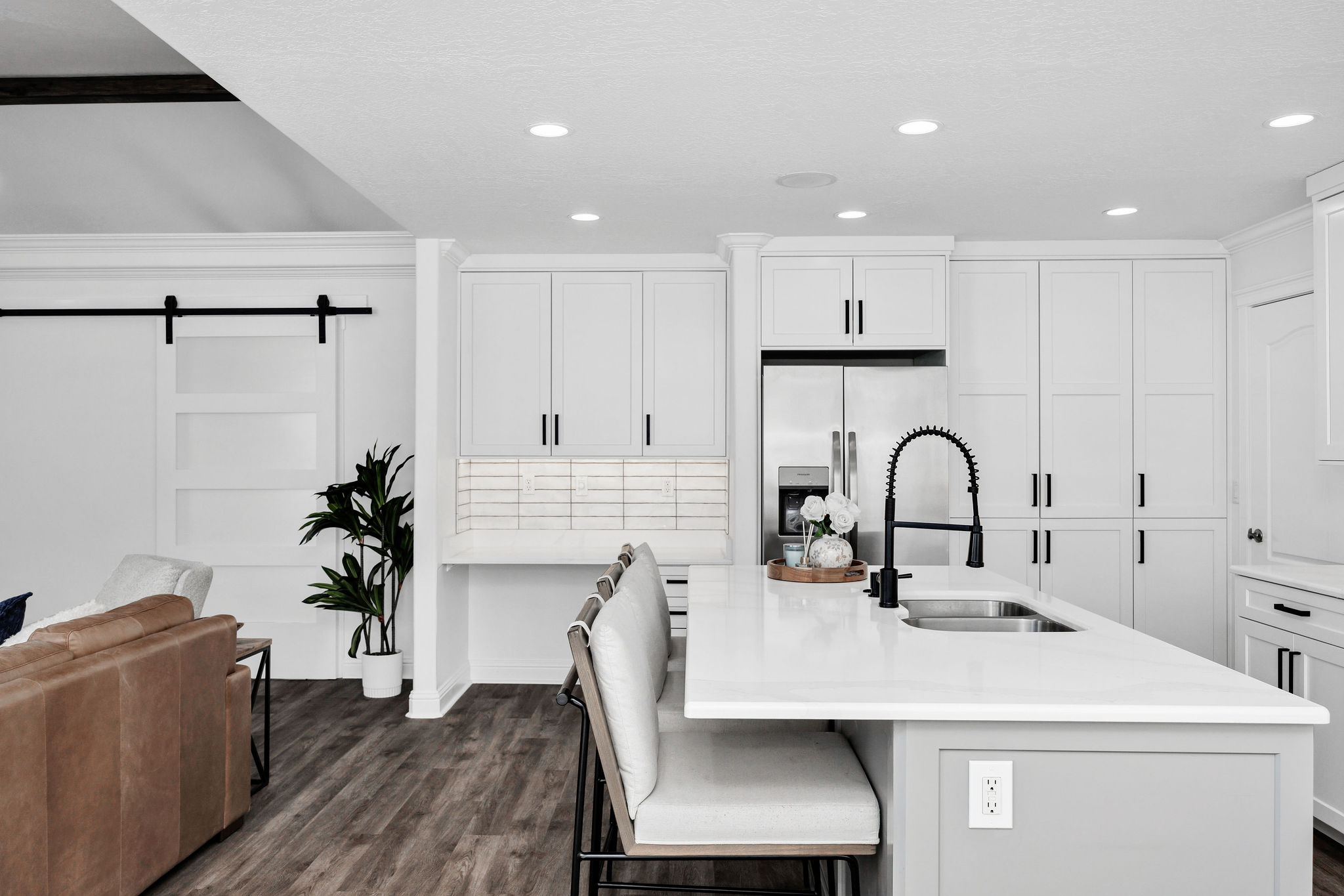 Modern kitchen featuring an expansive island with a built-in sink, white cabinetry, a subway tile backsplash, and stainless steel appliances