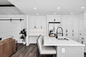Modern kitchen featuring an expansive island with a built-in sink, white cabinetry, a subway tile backsplash, and stainless steel appliances