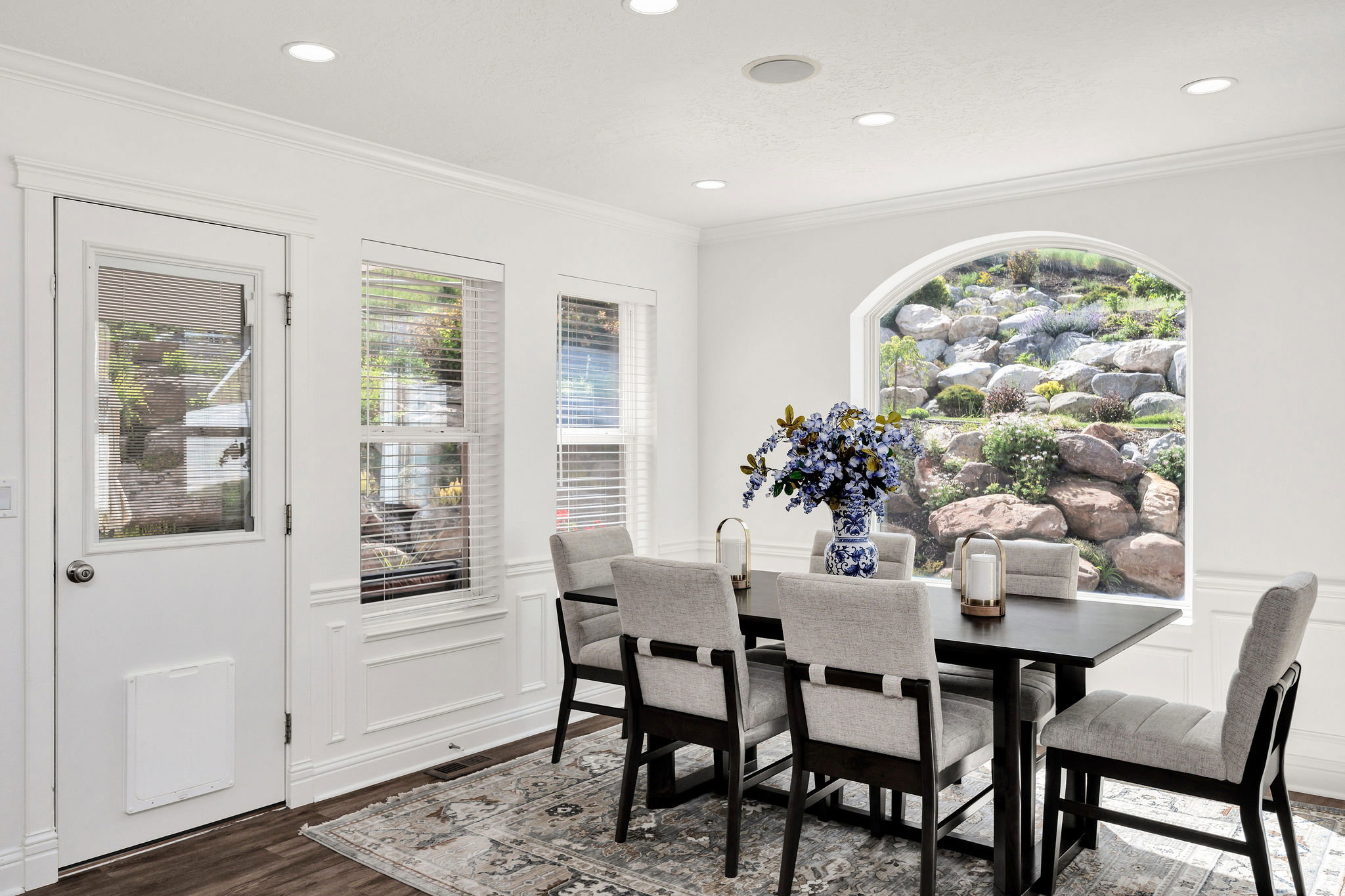 White wall paneling with an arched window, recessed lighting, crown molding, and wood-finish flooring