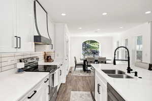 White cabinetry with matte black hardware, a custom range hood, subway tile backsplash, and white countertops