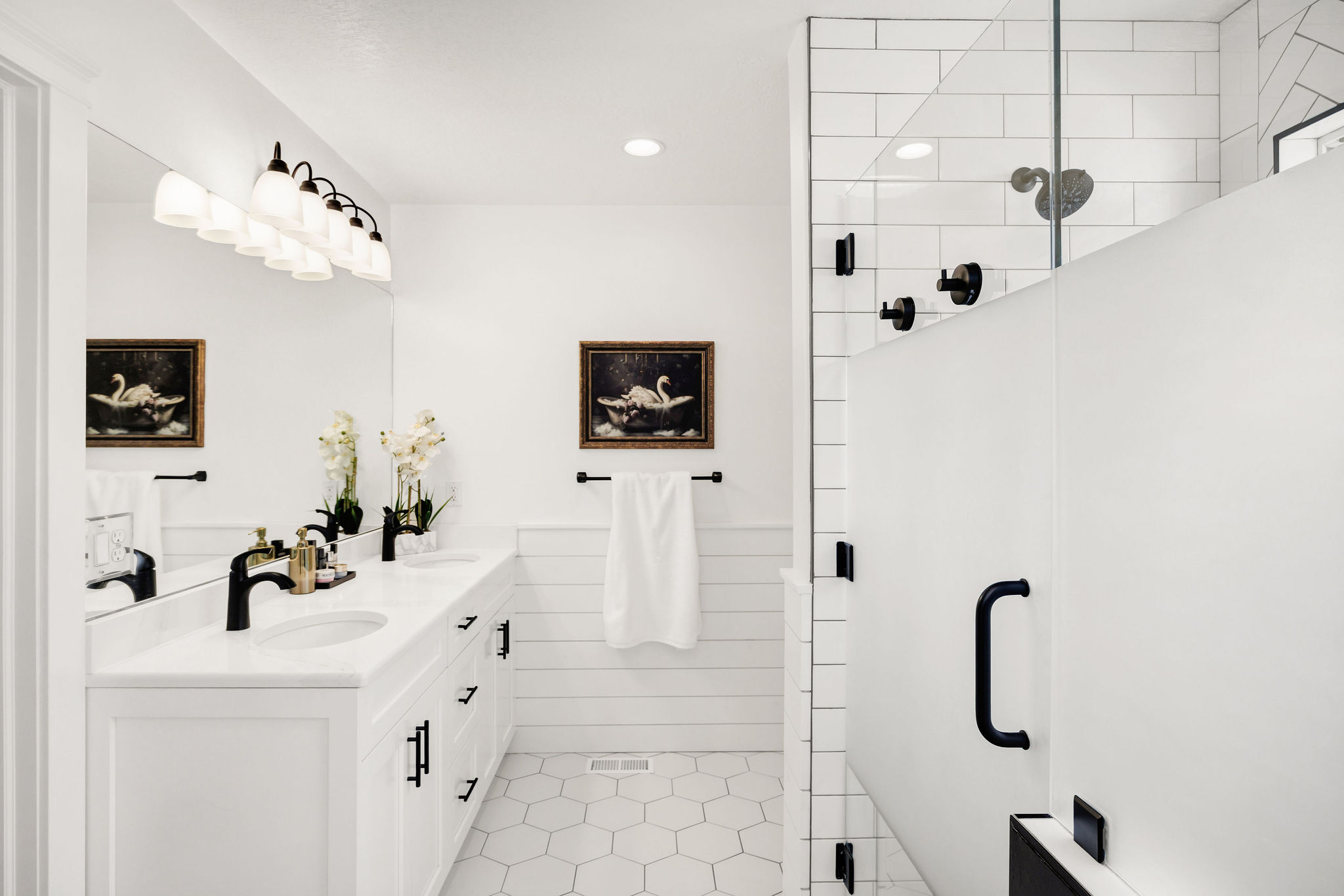 Spacious bathroom featuring a dual vanity with white cabinetry and countertops, matte black faucets, and a large mirror