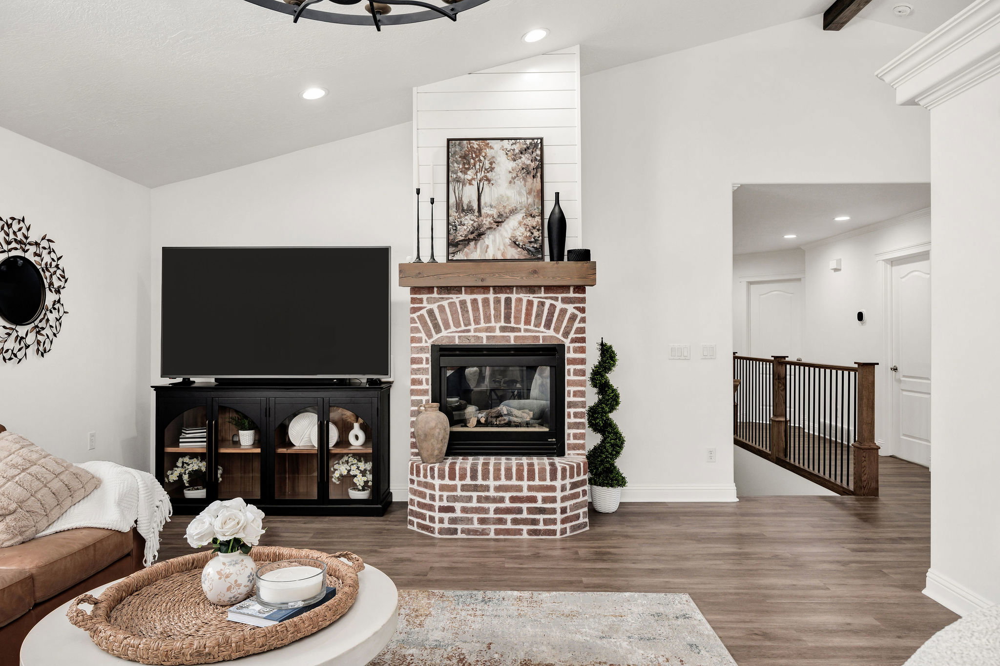 Brick fireplace with a substantial wood mantel, vaulted ceiling, wood-finish flooring, recessed lighting, and a wood staircase featuring black balusters