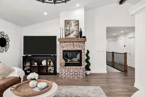 Brick fireplace with a substantial wood mantel, vaulted ceiling, wood-finish flooring, recessed lighting, and a wood staircase featuring black balusters