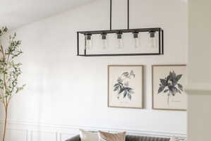 Linear chandelier with a black frame and clear glass shades, illuminating a space with white walls and classic wainscoting