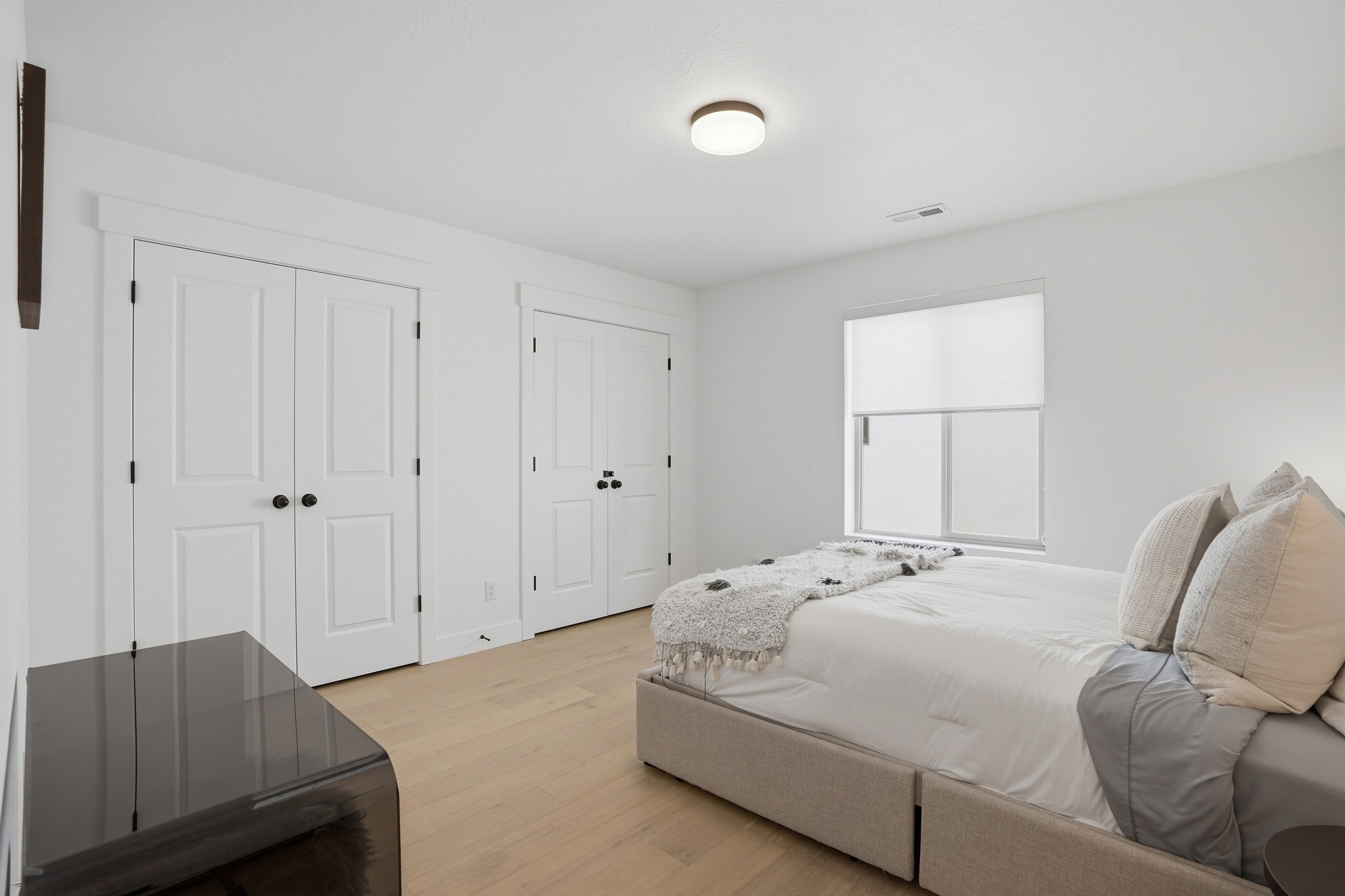 Bedroom featuring light wood-finish flooring, white walls, and a window with a roller shade