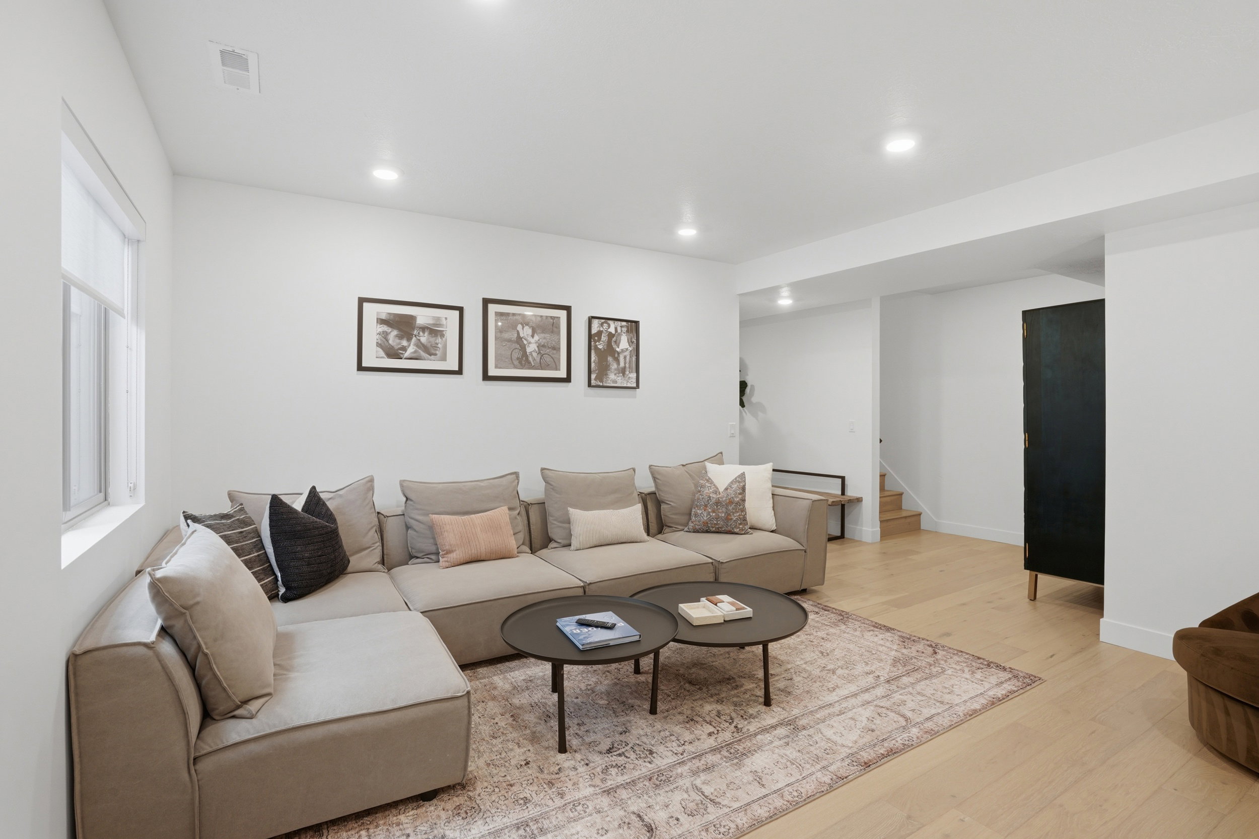 Spacious living area featuring light wood-finish flooring, recessed lighting, and a window with roller shades