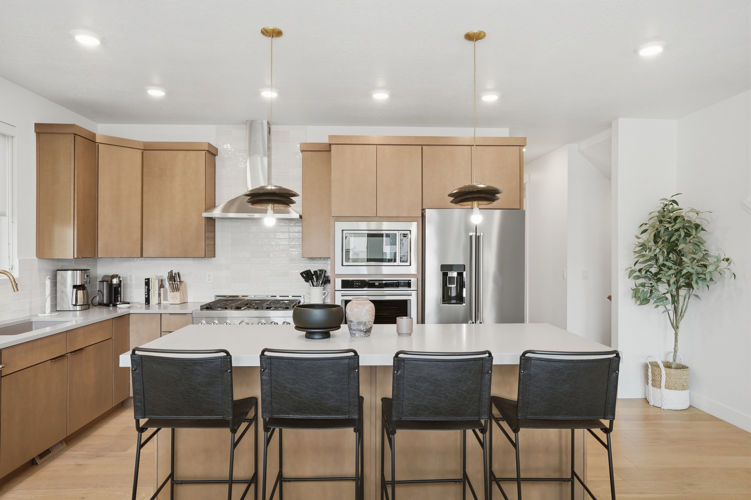 Modern kitchen featuring a central island with seating, stainless steel appliances, light wood-finish cabinetry, a subway tile backsplash, and recessed lighting