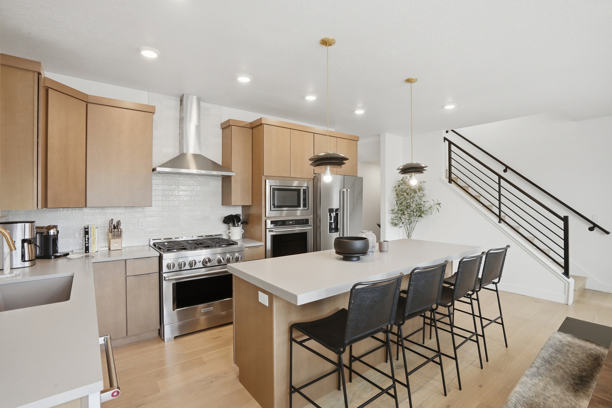 Open-concept kitchen featuring light wood-finish cabinetry, stainless steel appliances, a subway tile backsplash, a large center island with seating, and wood-finish flooring