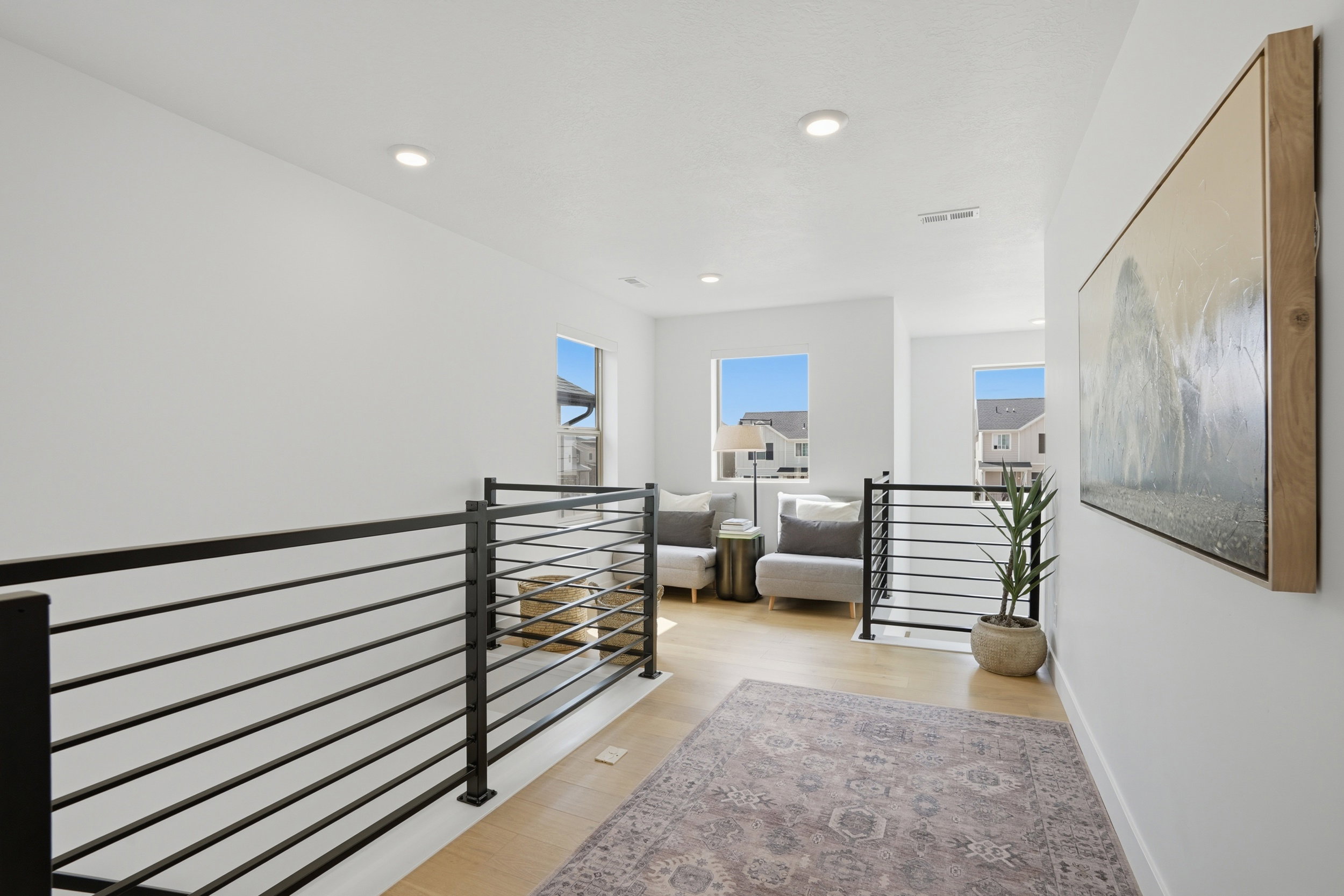 Upper-level landing featuring light wood-finish flooring, recessed lighting, and modern black horizontal bar railings