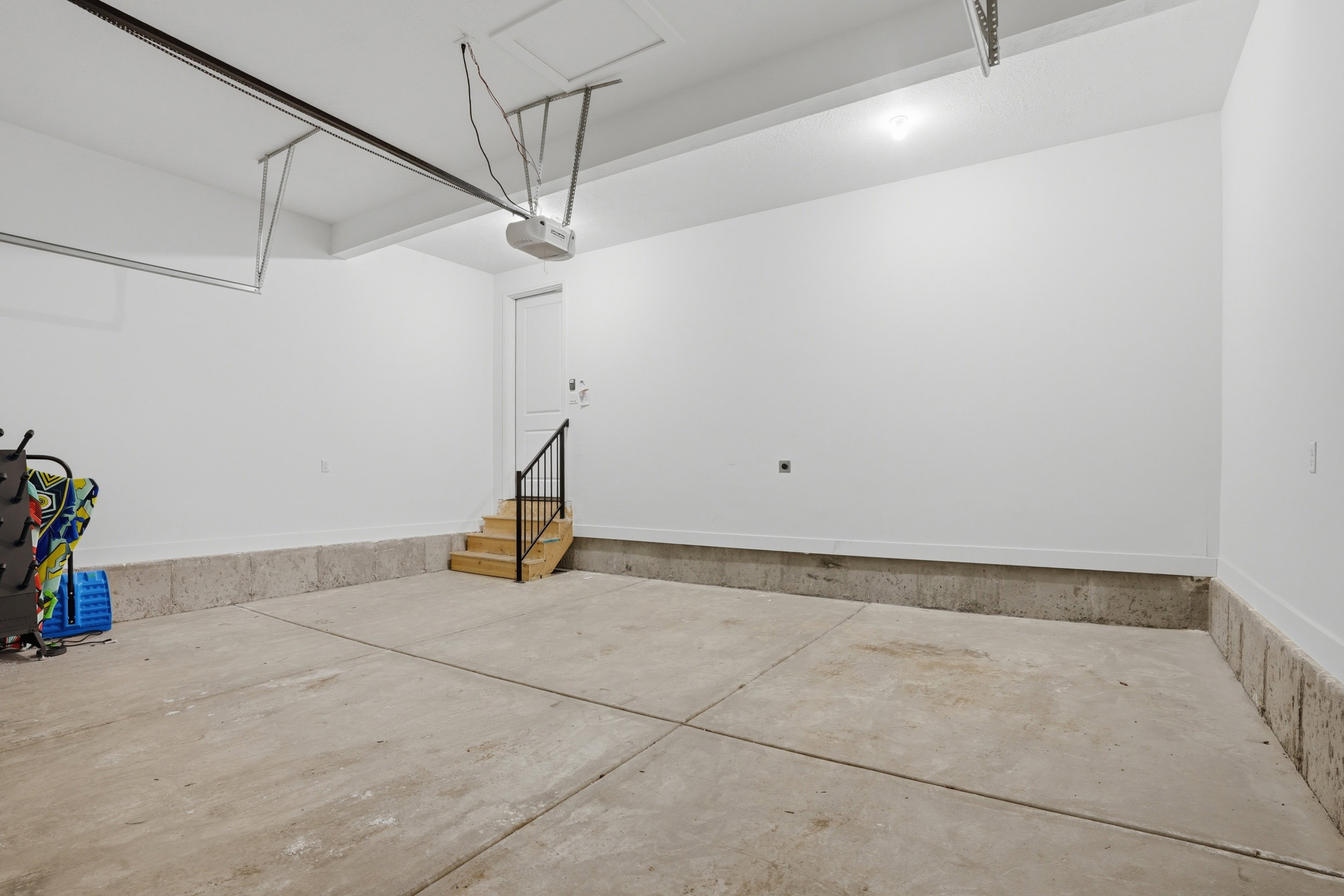 Spacious garage featuring a concrete floor, painted walls, overhead lighting, and a built-in wooden staircase with a metal railing
