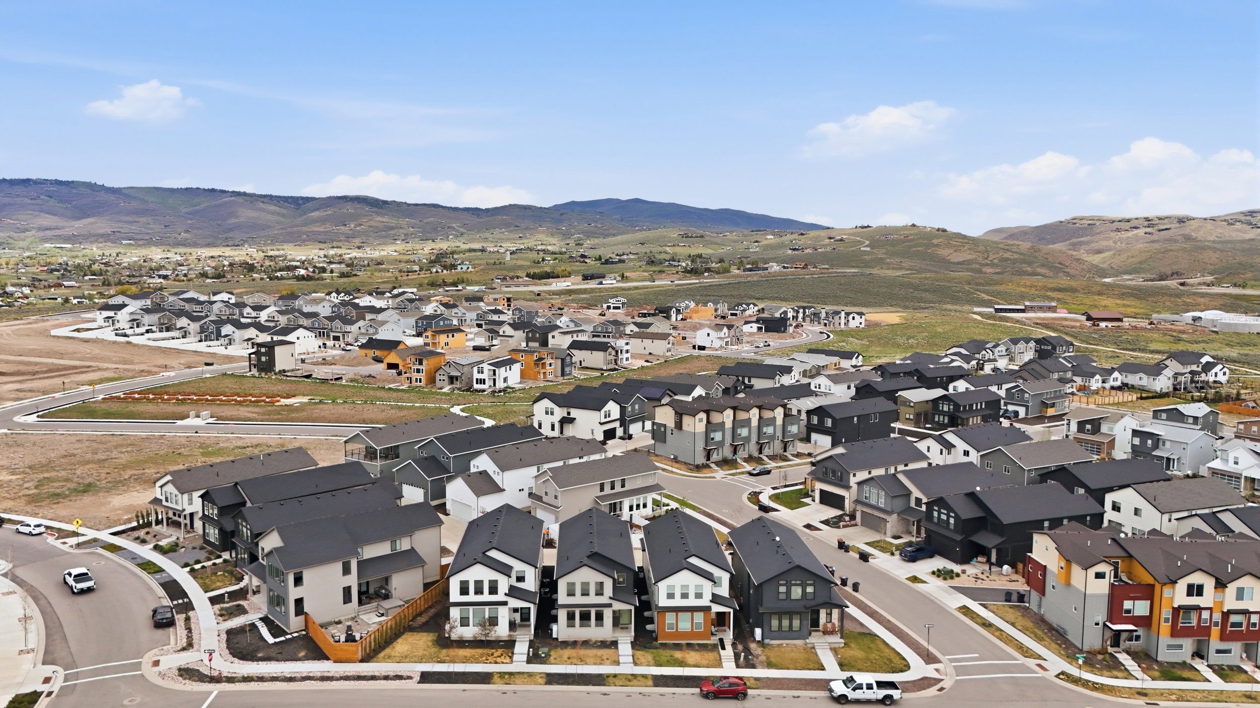 Aerial view of a residential community featuring diverse architectural styles, paved streets, and mountainous terrain in the background