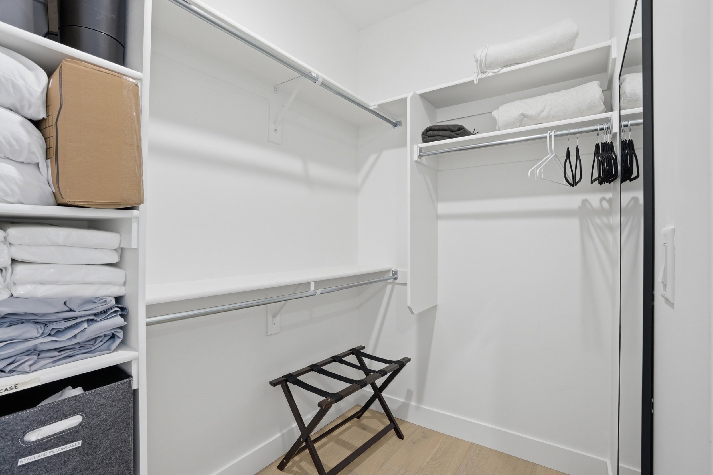 Walk-in closet featuring white built-in shelving, multiple hanging rods, and wood-finish flooring