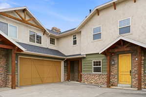 Exterior featuring stucco and river stone accents, a prominent garage with a wood-finish door, and a covered entry with a distinctive yellow front door