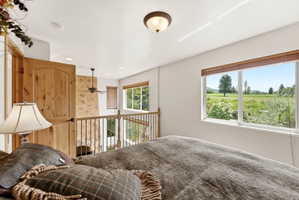 Loft space featuring a natural wood panel door, iron baluster railing, and ceiling fan
