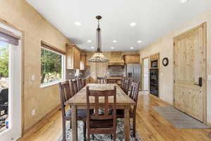 Spacious kitchen and dining area featuring wood-finish flooring, recessed lighting, wood cabinetry, a tile backsplash, and stainless steel appliances