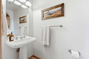 White pedestal sink with a dual-handle faucet, illuminated by a four-light vanity fixture
