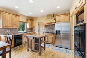 Kitchen featuring light wood cabinetry, a decorative range hood, stainless steel side-by-side refrigerator, and hardwood flooring