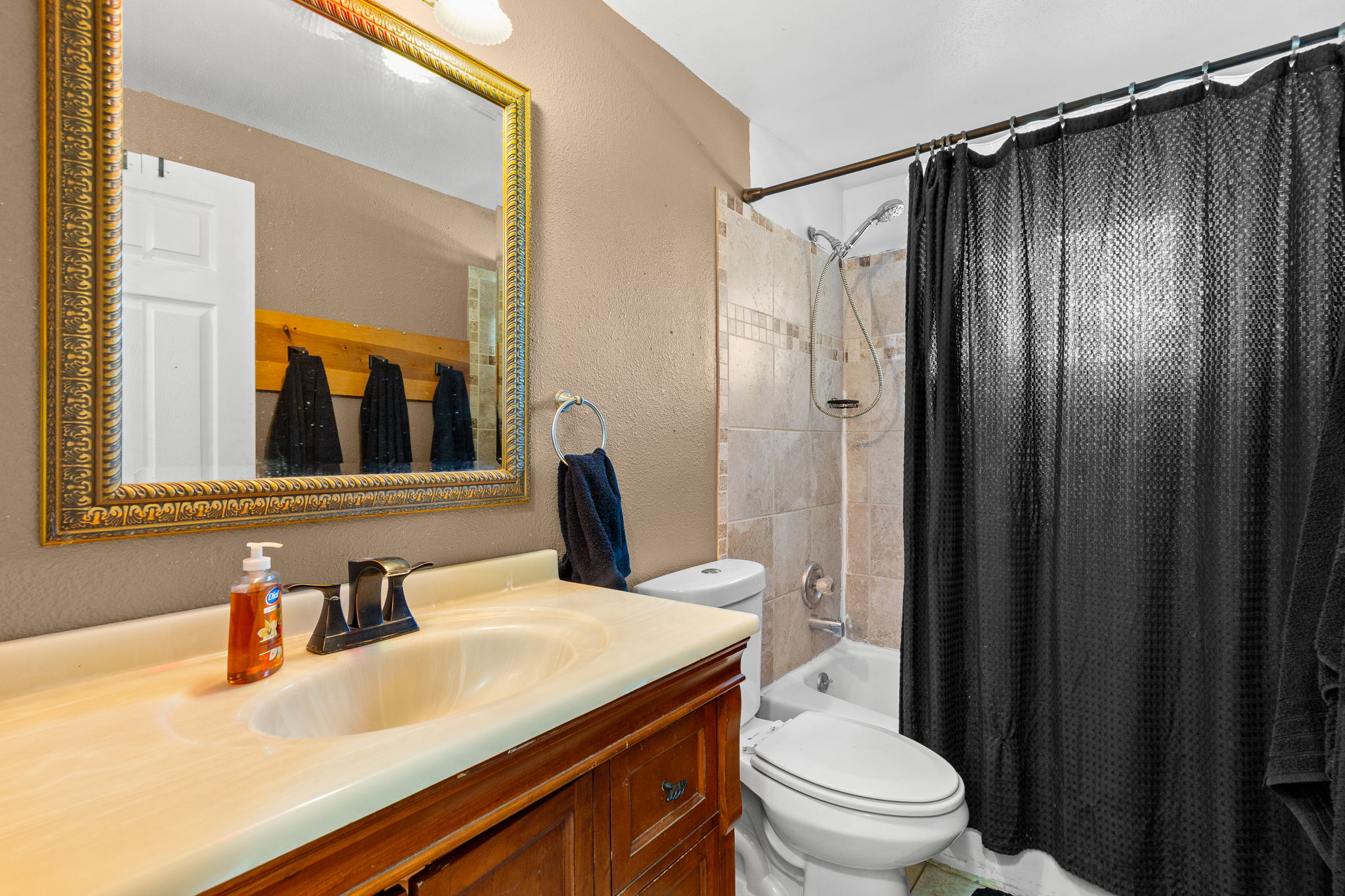 Full bathroom featuring a wood-finish vanity with an integrated sink, an ornate gold-framed mirror, and a tiled shower-tub combination