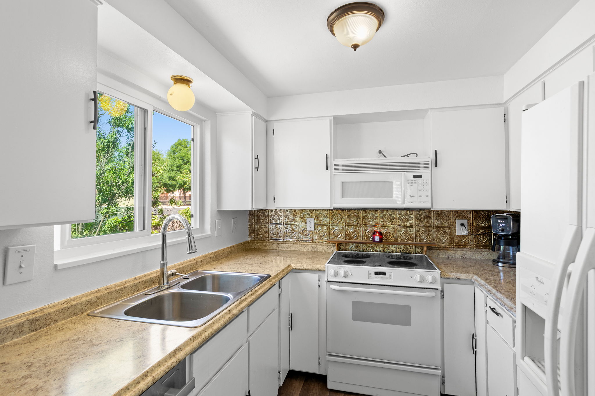 Kitchen featuring white cabinetry, a double basin stainless steel sink, patterned tile backsplash, and light-toned countertops