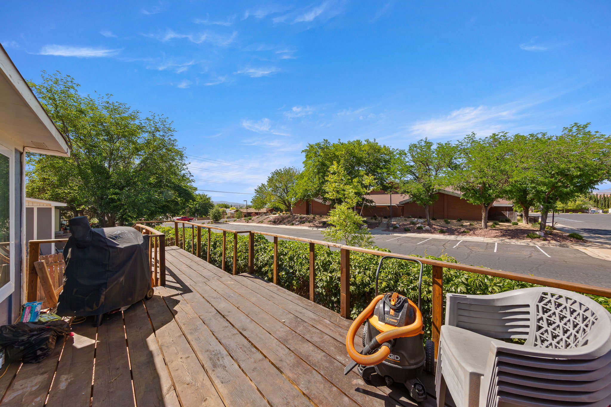 Expansive wood-finish deck with wood railings, surrounded by mature trees and landscaping