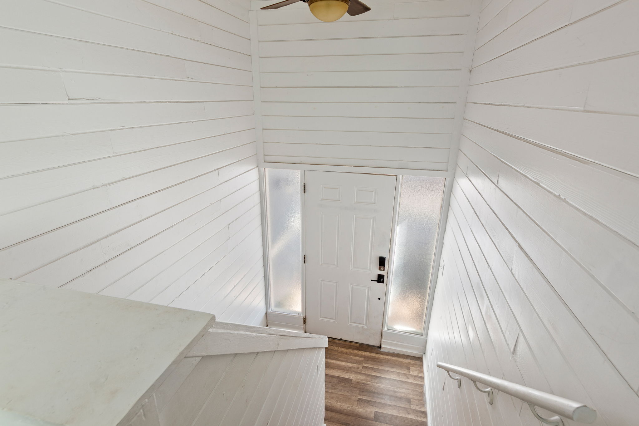 Entryway featuring wood-finish flooring, a white paneled door with frosted glass sidelights, and a ceiling fan