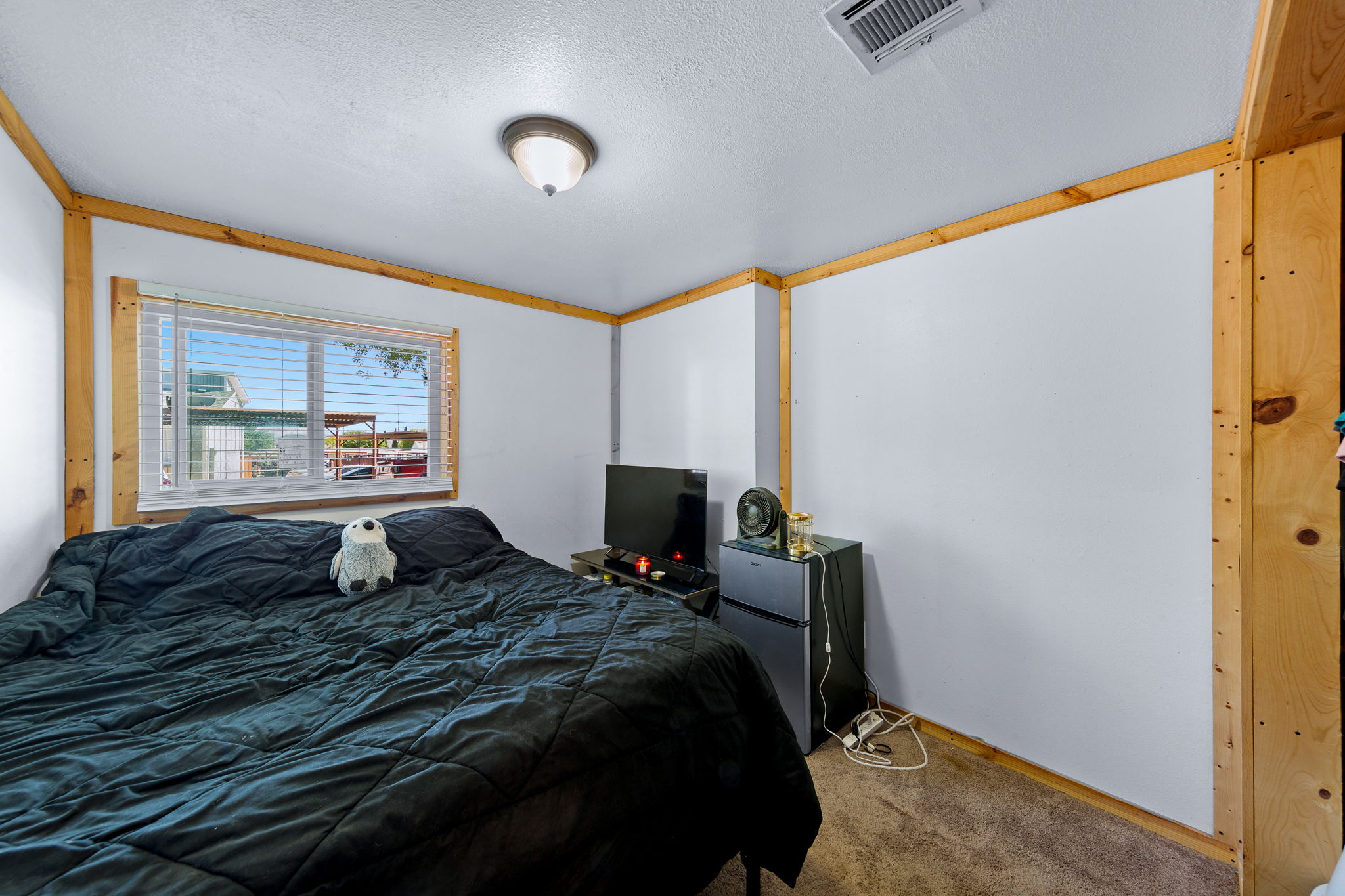 Carpeted room with a ceiling-mounted light fixture, visible window with blinds, and wood trim detailing