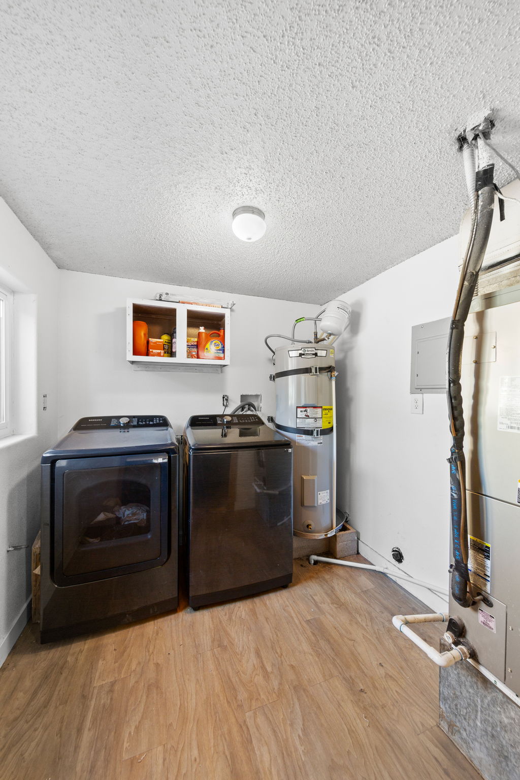 Utility area featuring wood-finish flooring, a water heater, and a white storage cabinet