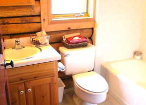 The main floor bath features a pine vanity, pine medicine cabinet, & casement window with red Roman shade.