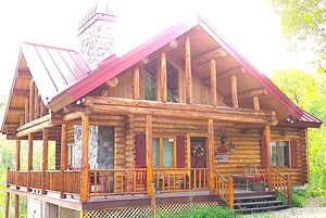 Log home exterior featuring a red metal roof, full-width covered porch, stone chimney, log construction, and red window shutters
